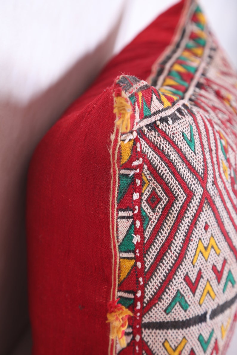 May include: Red throw pillow with a geometric pattern in white, yellow, green, and black. The pillow has a fringe trim.