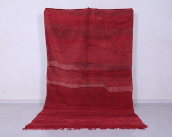 May include: A red woven rug with a striped pattern. The rug has a fringe border.
