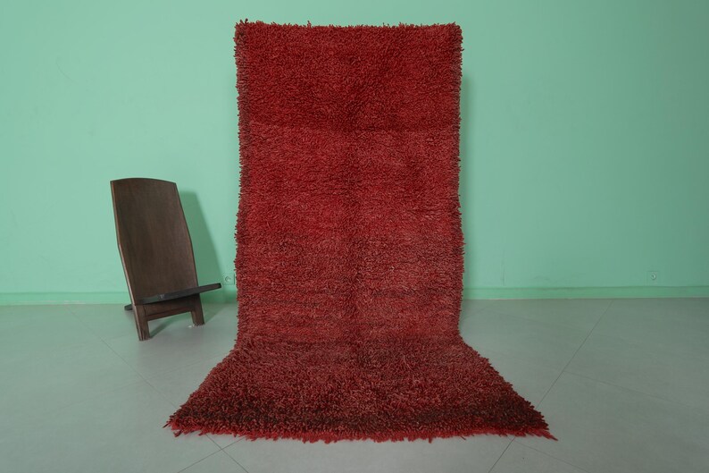 May include: A red shag rug with a long pile. The rug is laid out on a light green floor.