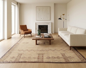 Op de afbeelding: Een moderne woonkamer met een beige tapijt met een geometrisch patroon. De kamer heeft een witte bank, een bruine leren fauteuil en een houten salontafel. Een open haard en grote ramen maken de scène compleet.
