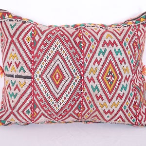 May include: A red, white, green, and yellow patterned throw pillow with tassels. The pillow is made of woven fabric and has a geometric design.