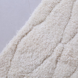 May include: A close-up of a white, fluffy, textured rug with a quilted pattern.