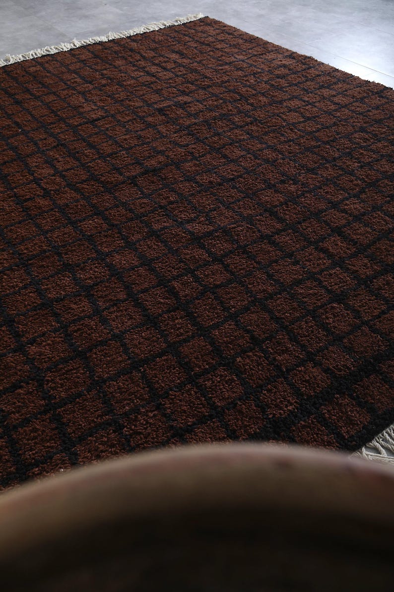 Peut inclure: Un tapis rectangulaire marron avec un motif quadrill&eacute; de lignes noires. Le tapis a une surface textur&eacute;e et moelleuse et une frange sur un bord. Le motif est un motif r&eacute;p&eacute;titif de carr&eacute;s.