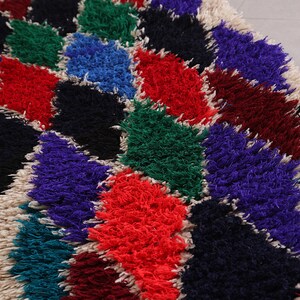 May include: A colorful, fluffy rug with a geometric pattern of diamonds in shades of red, blue, green, purple, black, and white.
