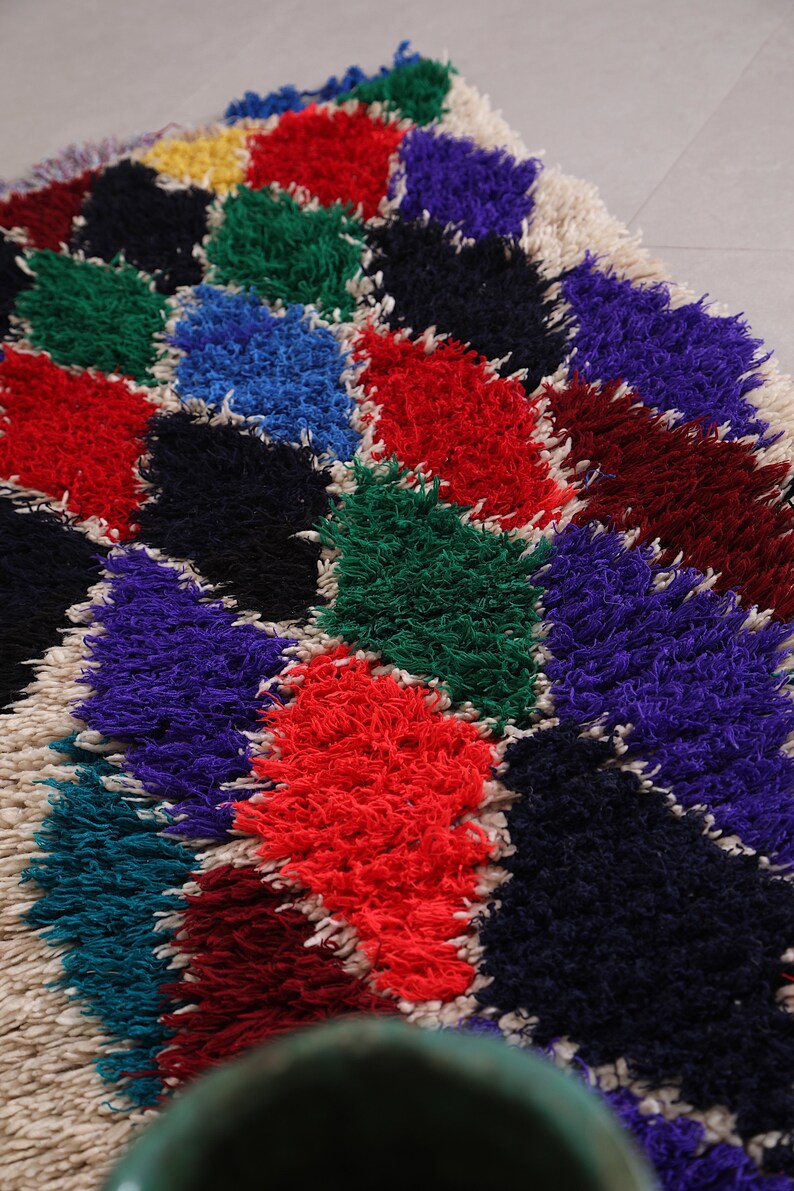 May include: A colorful, fluffy rug with a geometric pattern of diamonds in shades of red, blue, green, purple, black, and white.