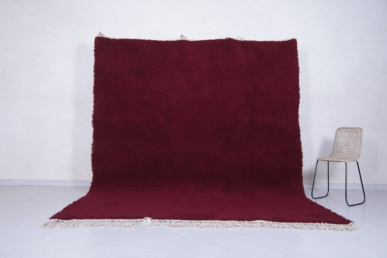 May include: A large, deep red, shag rug with a white fringe border. The rug is folded in half and laid flat on a white surface.