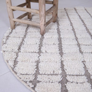 May include: A round, white and gray rug with a geometric pattern. The rug is made of fluffy, textured fibers and has a subtle sheen.