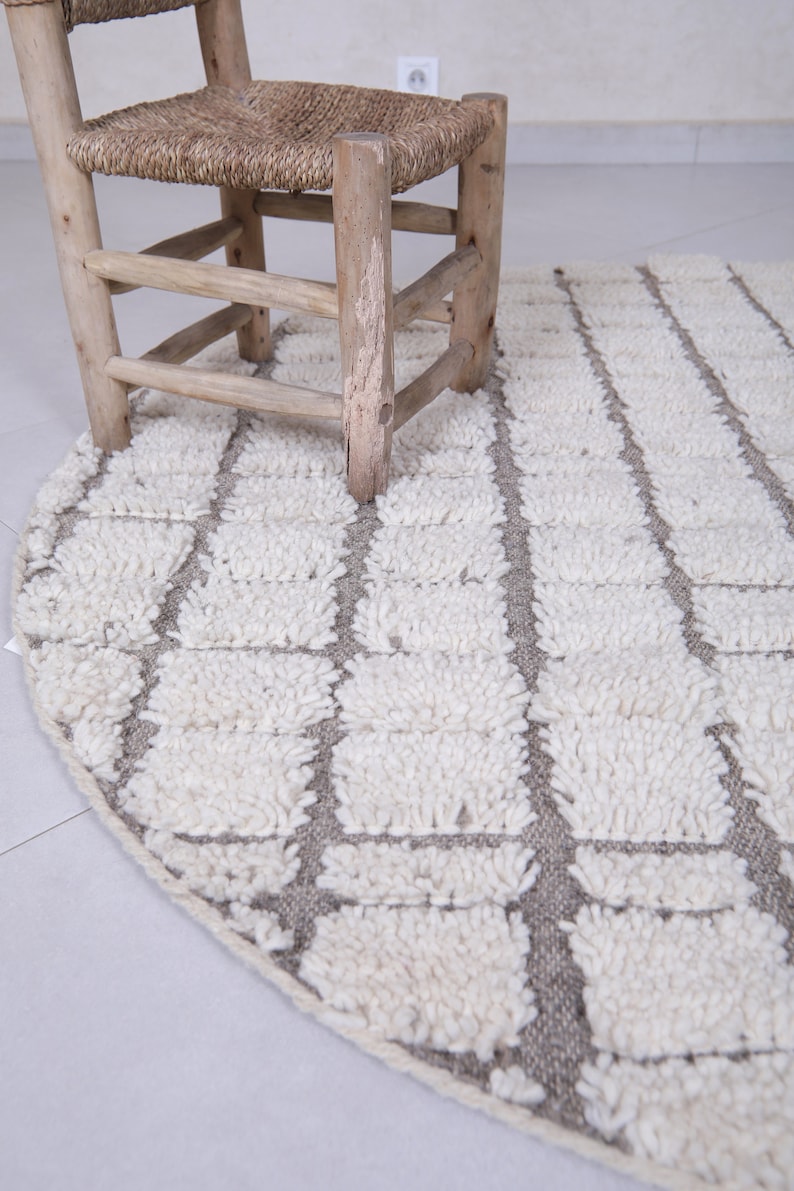 May include: A round, white and gray rug with a geometric pattern. The rug is made of fluffy, textured fibers and has a subtle sheen.