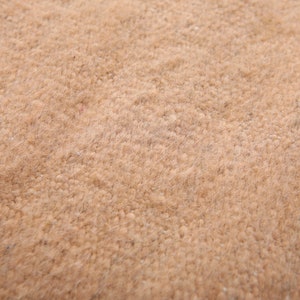 May include: Close-up of a light brown, textured fabric. The fabric has a soft, fuzzy appearance.