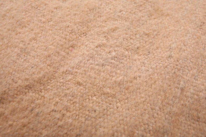 May include: Close-up of a light brown, textured fabric. The fabric has a soft, fuzzy appearance.