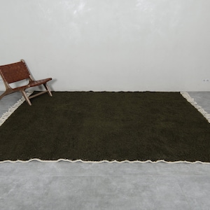 May include: A dark green shag rug with a white fringe border. The rug is laid out on a gray tiled floor.