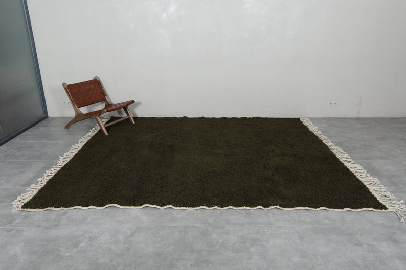 May include: A dark green shag rug with a white fringe border. The rug is laid out on a gray tiled floor.
