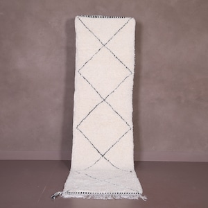 Op de afbeelding: Een witloperkleed met een zwart ruitpatroon. Het kleed heeft een franje rand.