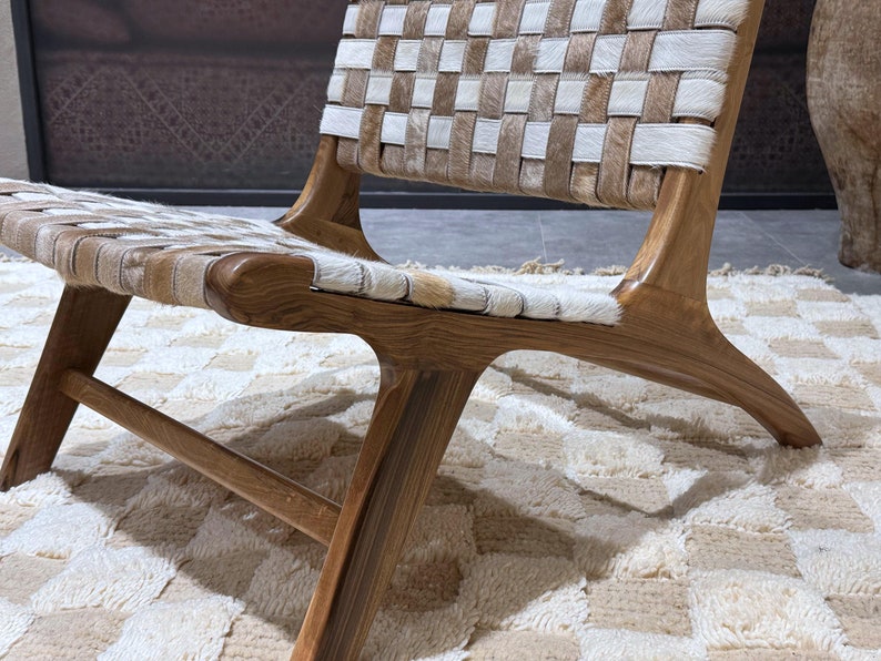 May include: A wooden chair with a woven leather seat and back. The chair has a natural wood finish and is sitting on a white and beige rug.