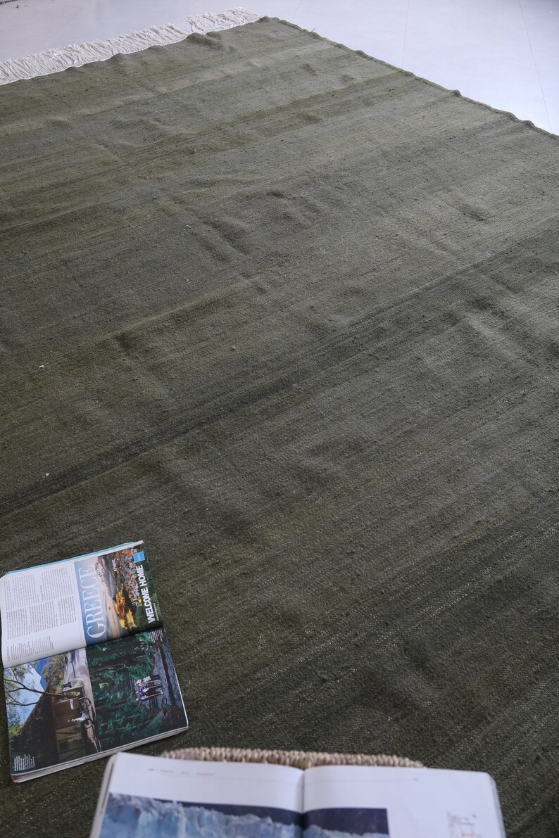 May include: A green wool rug with a subtle striped pattern. The rug is laid out flat on a white surface.