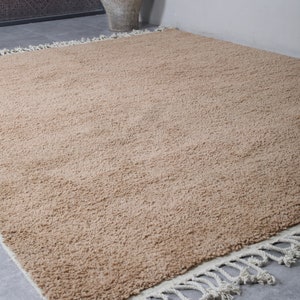 May include: A light brown shag rug with a white fringe border. The rug is made of a soft, fluffy material and has a subtle texture.