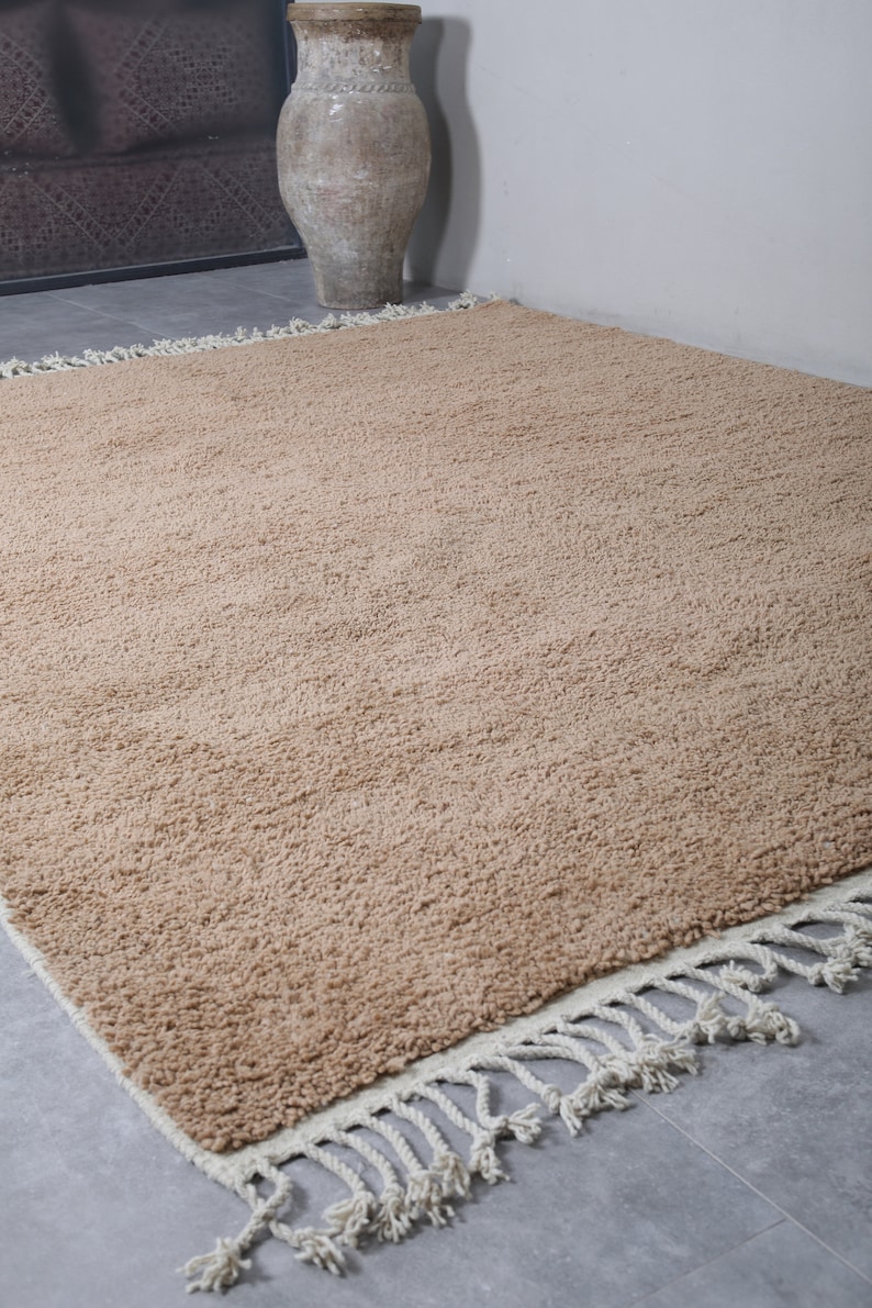 May include: A light brown shag rug with a white fringe border. The rug is made of a soft, fluffy material and has a subtle texture.