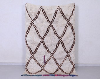 May include: Cream-colored, rectangular rug with a repeating brown diamond pattern. The rug has a shaggy texture and a colorful fringe at the bottom. A small section of the rug is damaged near the bottom.
