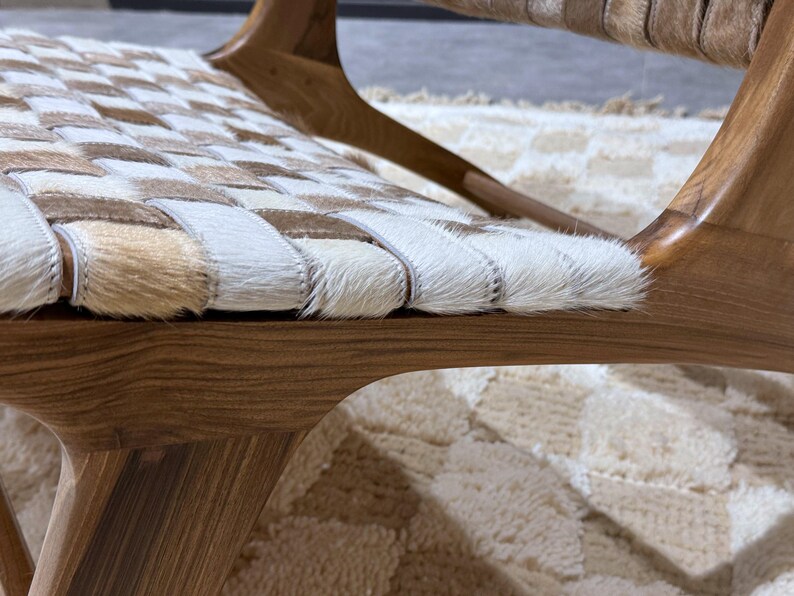 May include: Close-up of a wooden chair with a woven leather seat. The chair is brown and has a natural wood finish. The seat is made of white and brown leather strips woven together.