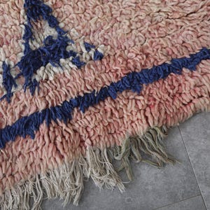 May include: A pink and blue handwoven rug with fringe. The rug has a geometric pattern with a blue and white design.