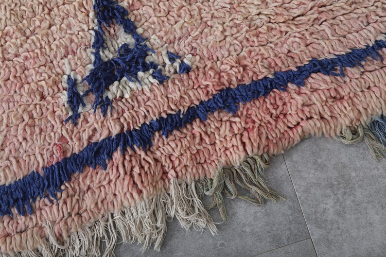 May include: A pink and blue handwoven rug with fringe. The rug has a geometric pattern with a blue and white design.