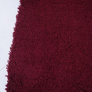 May include: Close-up of a deep red, plush bath mat with a soft, fluffy texture.