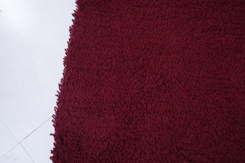 May include: Close-up of a deep red, plush bath mat with a soft, fluffy texture.
