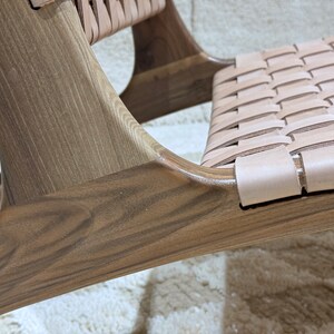 May include: Close-up of a wooden chair with a woven leather seat. The chair has a dark brown stain and a natural wood grain. The leather seat is light brown and has a woven pattern.