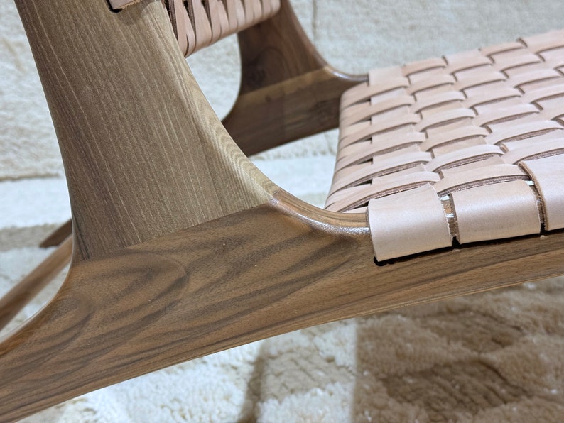 May include: Close-up of a wooden chair with a woven leather seat. The chair has a dark brown stain and a natural wood grain. The leather seat is light brown and has a woven pattern.