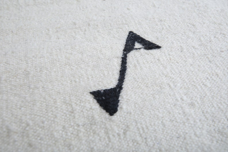 Może przedstawiać: Czarny symbol nuty muzycznej wyszyty na białym materiale.