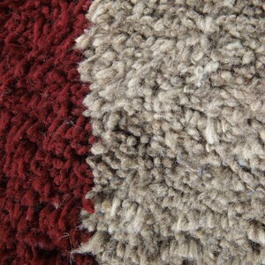 May include: Close-up of a textured rug with a thick, shaggy pile. The rug features a bold design with a deep burgundy red on the left and right sides, and a wide stripe of light gray in the center. The fibers are dense and create a soft, inviting look.