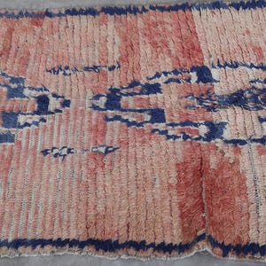 May include: A hand-woven rug with a geometric pattern in shades of pink, blue, and white. The rug has a distressed, vintage look and is made of natural fibers.