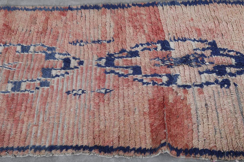 May include: A hand-woven rug with a geometric pattern in shades of pink, blue, and white. The rug has a distressed, vintage look and is made of natural fibers.