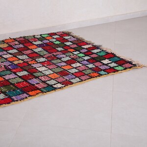 May include: A colorful Moroccan rug with a checkered pattern in shades of red, orange, green, blue, and purple. The rug has a fringe border and is made of wool.