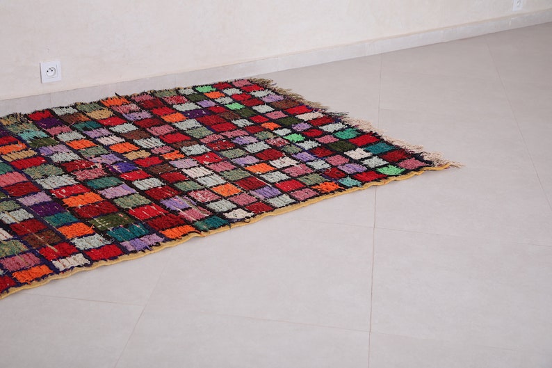 May include: A colorful Moroccan rug with a checkered pattern in shades of red, orange, green, blue, and purple. The rug has a fringe border and is made of wool.