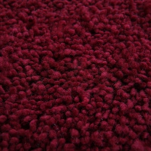 May include: Close-up of a deep red, fuzzy rug. The texture is made of small, densely packed loops of yarn.