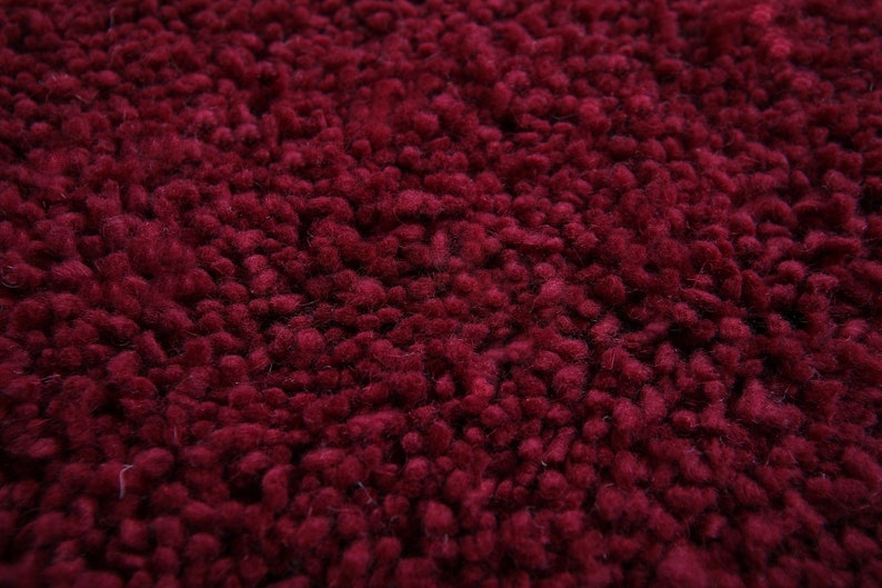 May include: Close-up of a deep red, fuzzy rug. The texture is made of small, densely packed loops of yarn.