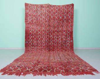 May include: A red Moroccan rug with a geometric pattern. The rug has a fringe border and is made of wool.