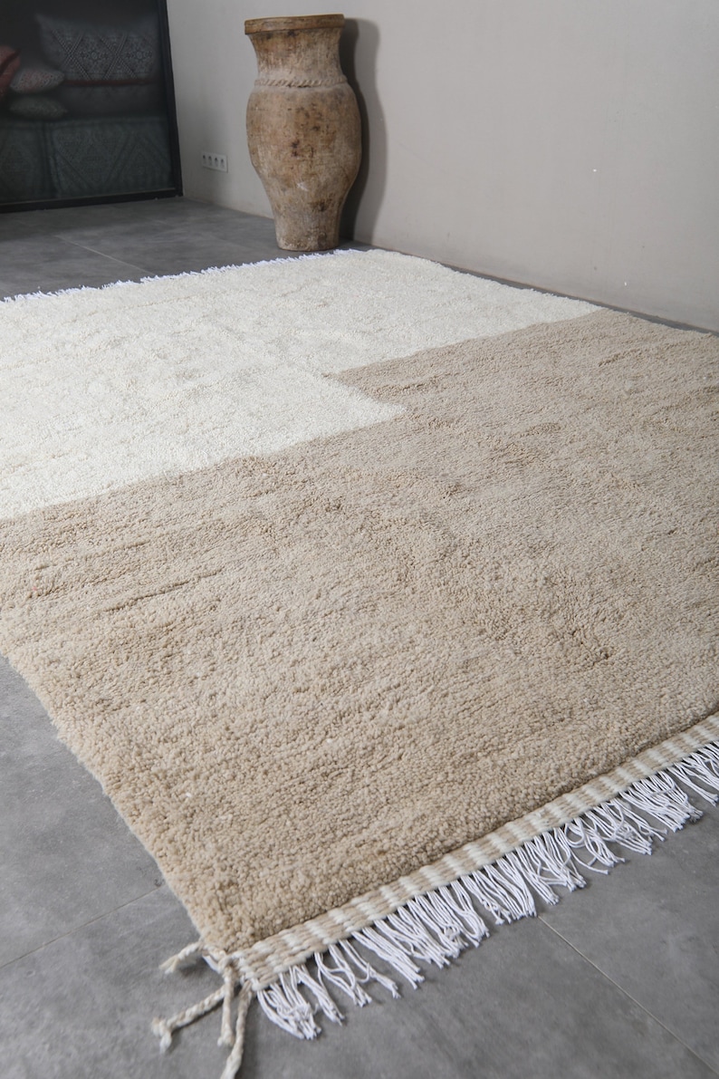 Puede incluir: Una alfombra beige y blanca con un borde de flecos. La alfombra est&aacute; hecha de un material suave y esponjoso.