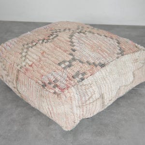 May include: A square, off-white floor cushion with a woven pattern in shades of pink and grey.