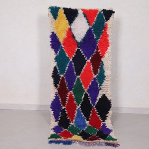 May include: A colorful Moroccan rug with a diamond pattern in shades of red, blue, green, yellow, and white. The rug has a fringe border and is made of wool.