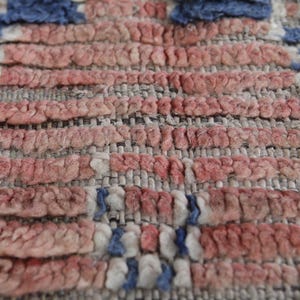 May include: Close-up of a woven rug with a red, white, and blue pattern. The rug is made of a thick, textured fabric and has a slightly distressed look.