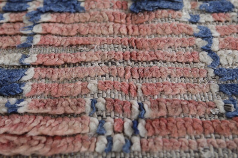 May include: Close-up of a woven rug with a red, white, and blue pattern. The rug is made of a thick, textured fabric and has a slightly distressed look.