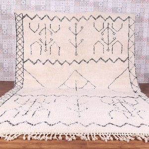 May include: A white Moroccan rug with black geometric patterns. The rug has a fringe border and is made of wool.