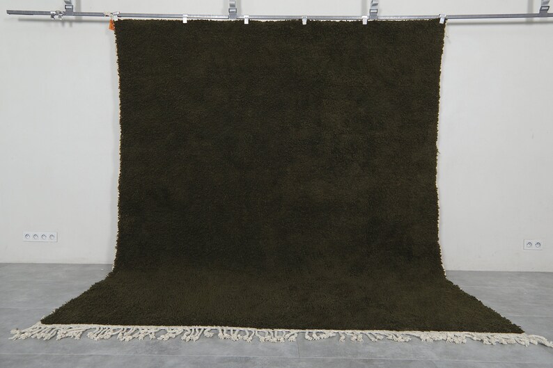 May include: A solid dark green rug with a fringe border. The rug is hanging from a metal rod.