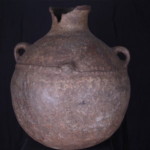 Peut inclure: Un grand pot en terre cuite brun avec deux anses. Le pot a un corps large et rond et un col étroit. Le col est ébréché et cassé.