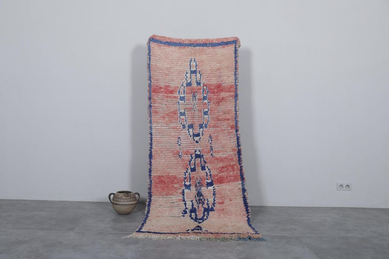 May include: A long, rectangular rug with a faded pink and white background. The rug has a blue and white geometric pattern in the center.