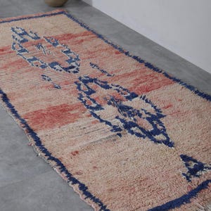 May include: A pink and blue Moroccan rug with a geometric pattern. The rug has a fringe border and is made of wool.