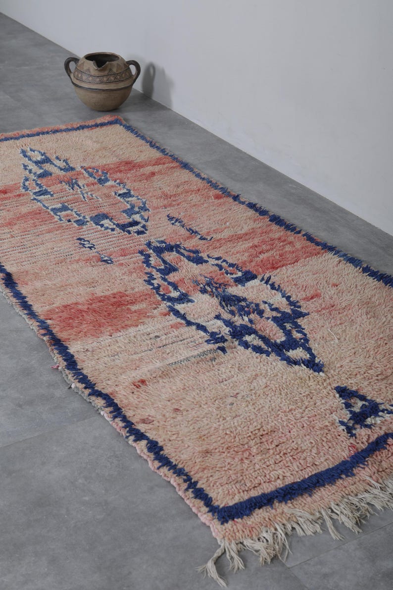 May include: A pink and blue Moroccan rug with a geometric pattern. The rug has a fringe border and is made of wool.