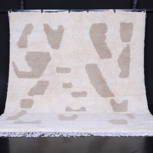 May include: A white and beige shag rug with an abstract pattern. The rug has a fringe border.